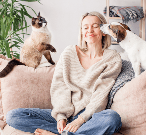 Women sitting on a sofa with cat sitting on the left and dog on the right 